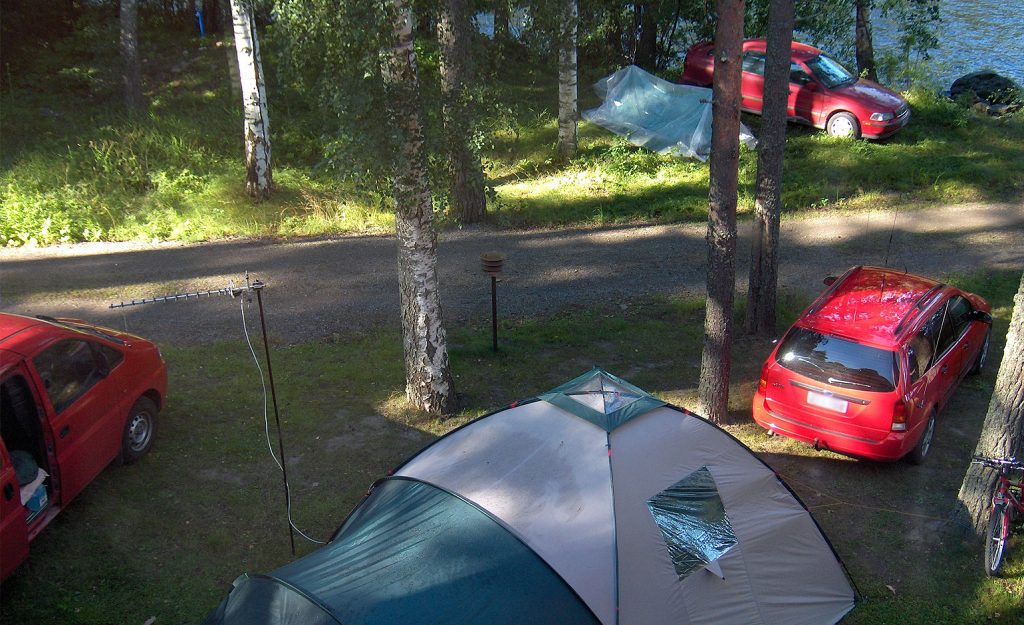 Telttoja, autoja ja antenneita järven rannalla.
